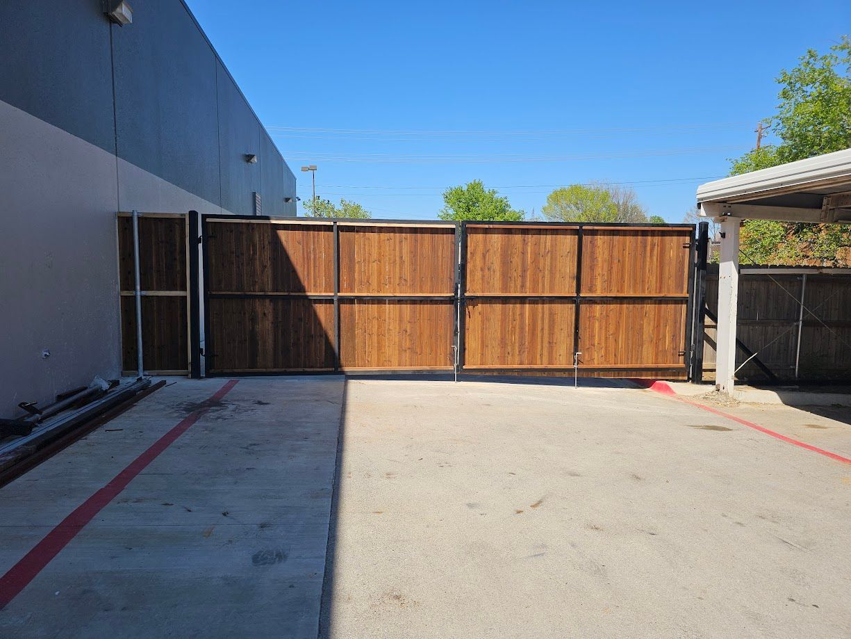 Empty concrete driveway with a large wooden gate and a white building on the left under a blue sky