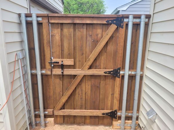 Wooden gate with diagonal brace and black hinges between two gray house walls