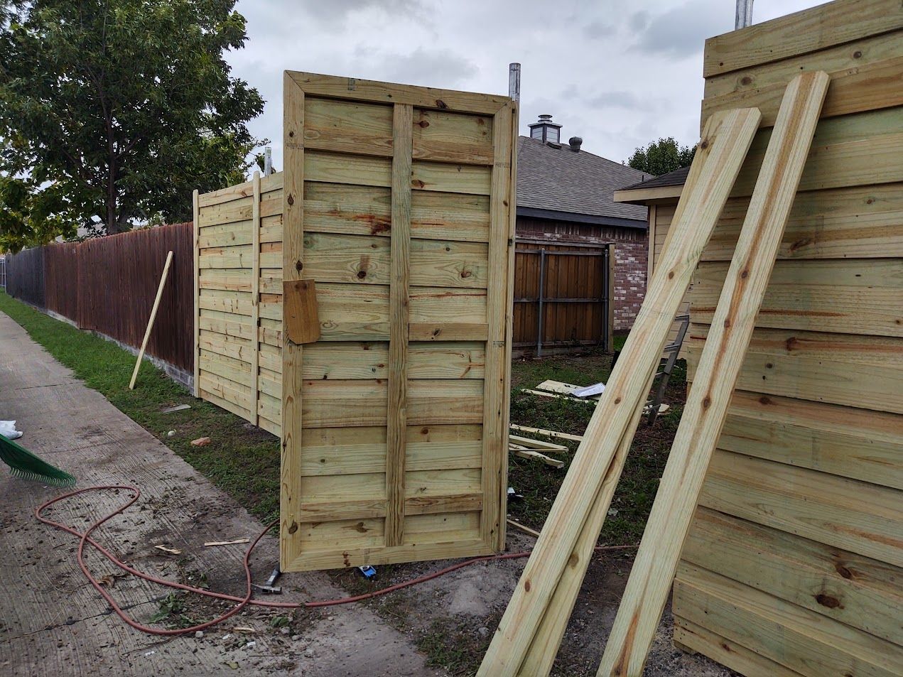 Wooden fence panels and gate sections stacked outdoors beside a house
