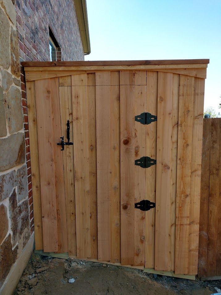 Wooden gate with black hinges beside a brick wall, outdoors in a narrow passage