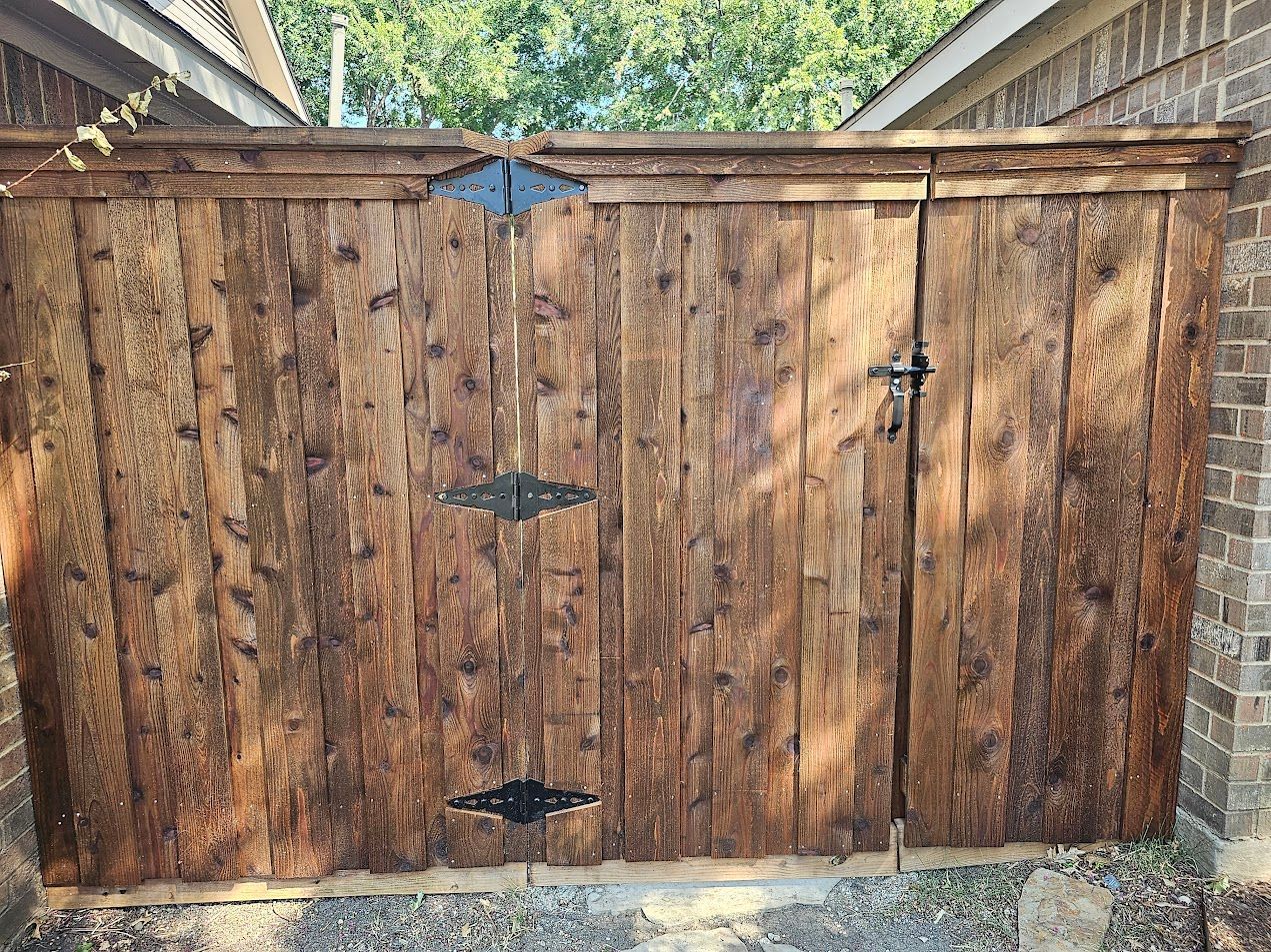 Rustic wooden double gate with metal hinges and latch, set between brick pillars and a stone path