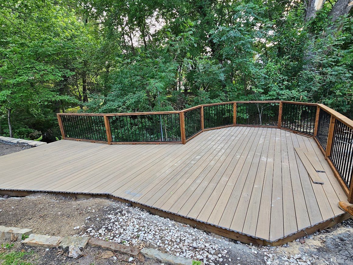 Wooden deck overlook with railings surrounded by dense green trees and gravel path nearby