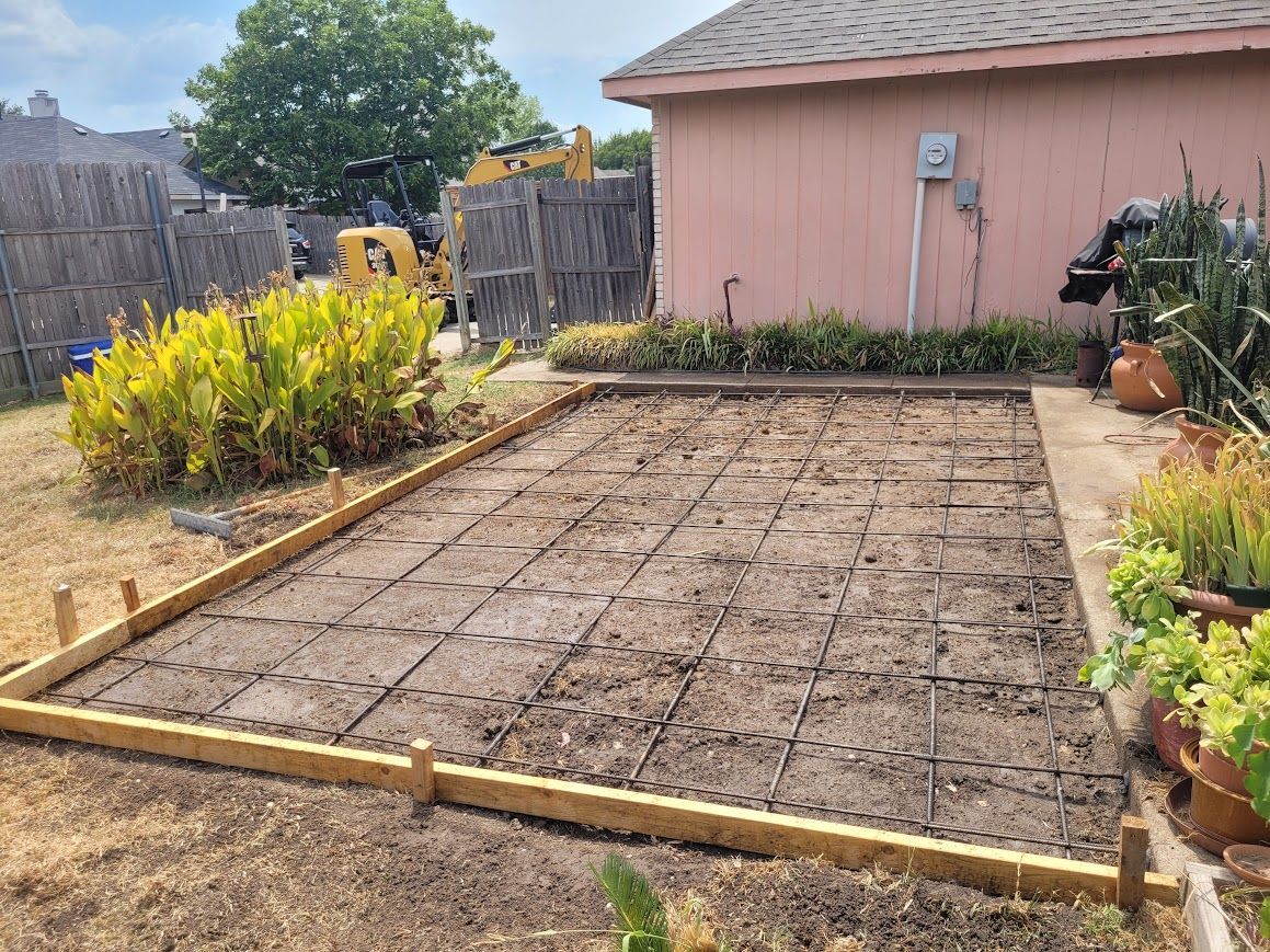 Bare garden bed framed by wood in a backyard beside a pink shed and fence