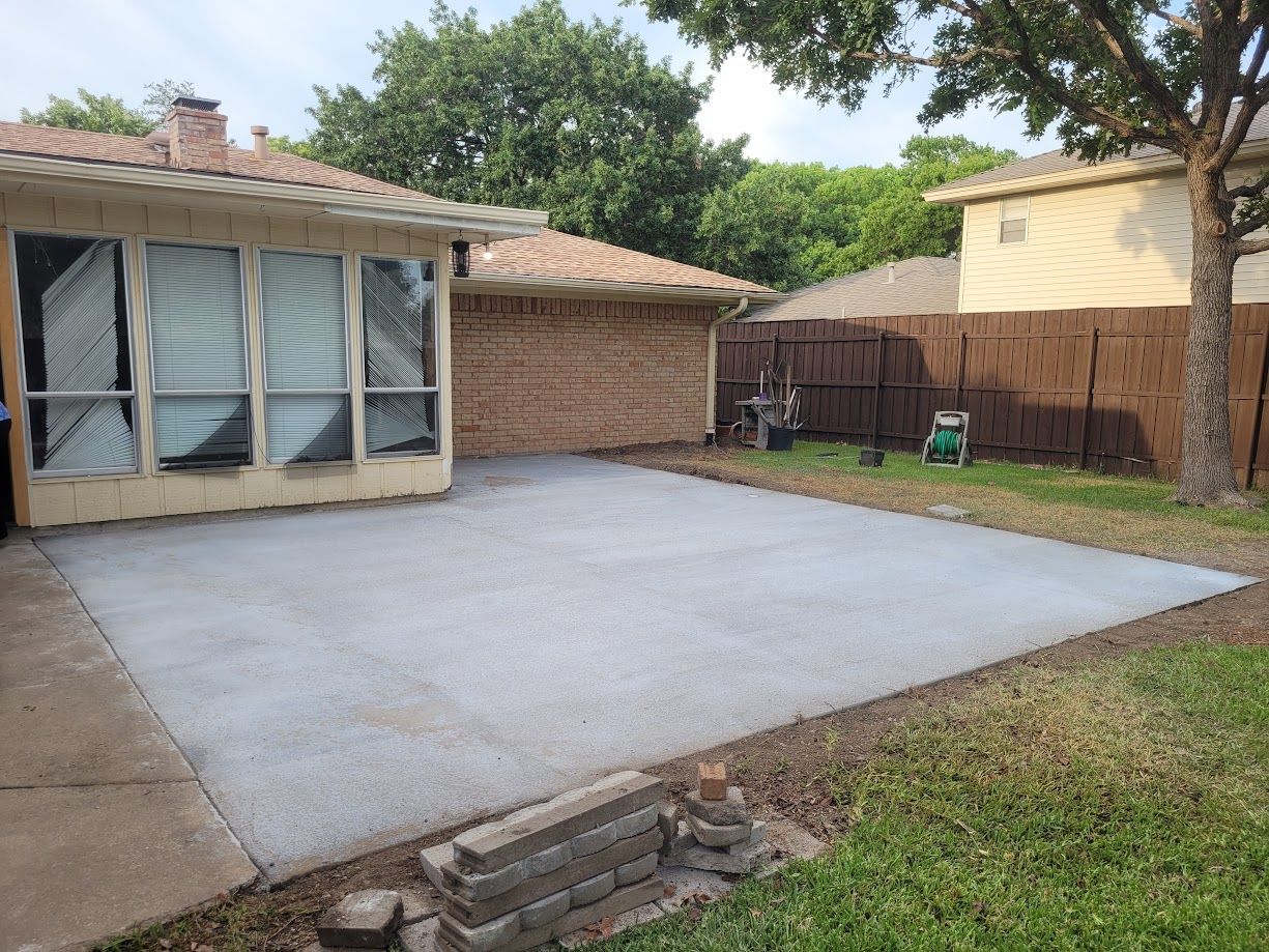 Backyard concrete patio beside a brick house, with sliding doors and a fenced yard.