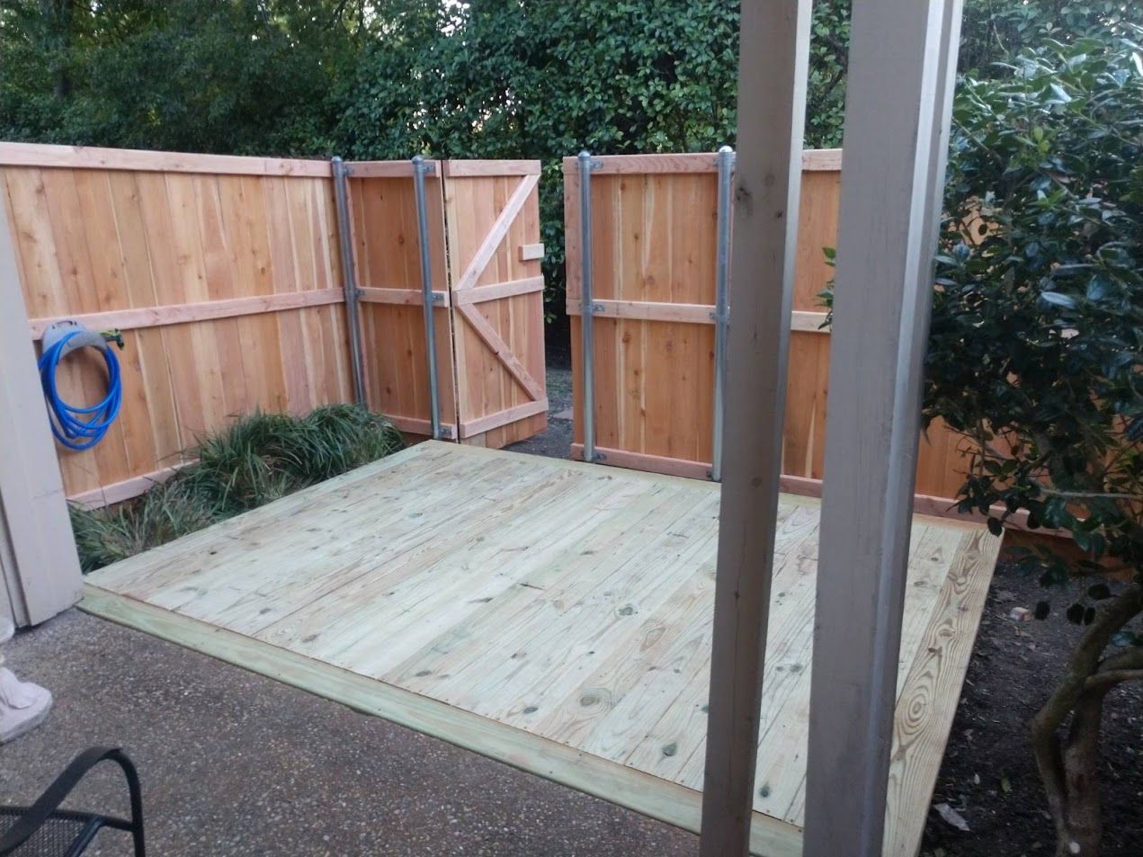 Wooden patio under construction beside a fenced yard, with a gate and stacked materials.