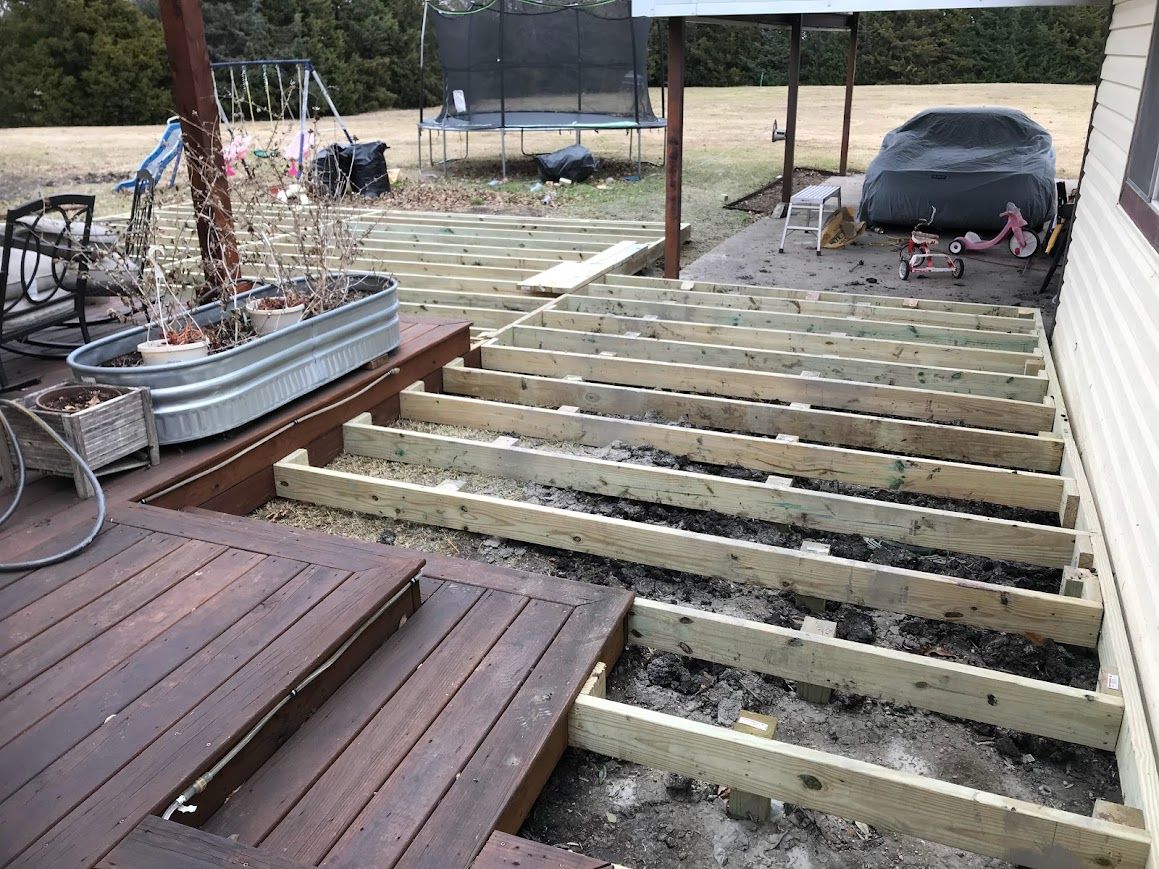 Raised deck frame with exposed joists beside a parked black car and a metal planter