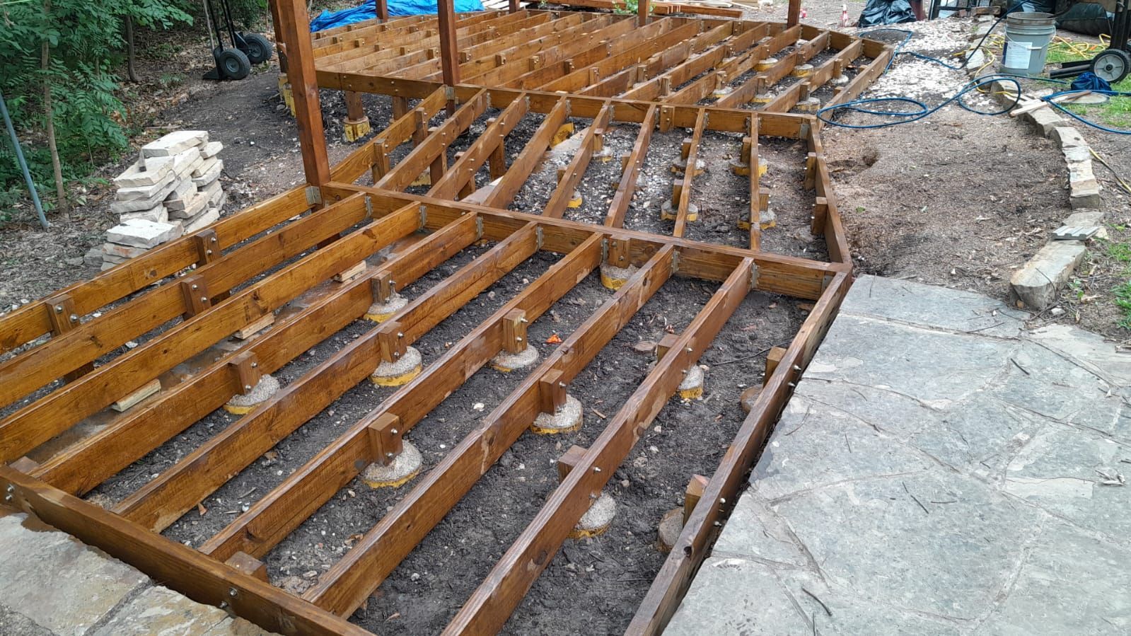Broken wooden deck framing beside a concrete path, with exposed joists and a damaged section