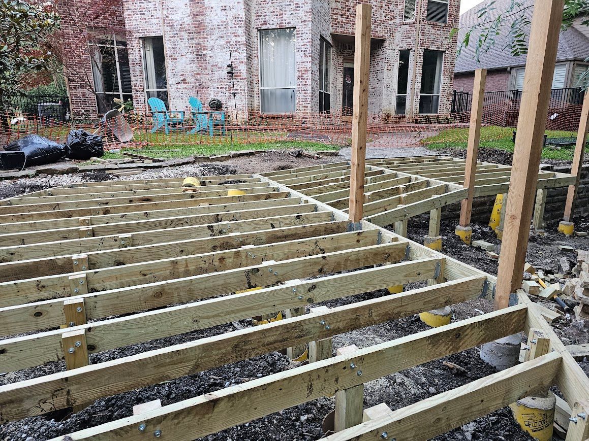 Wooden deck framing under construction in a brick courtyard with tools and materials nearby