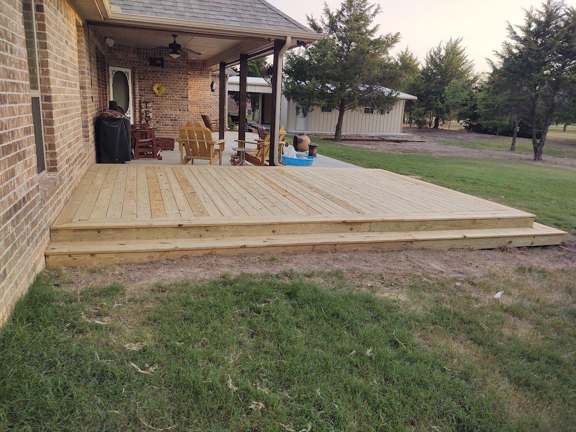 Back porch with a new wooden deck extension beside a brick house and grassy yard