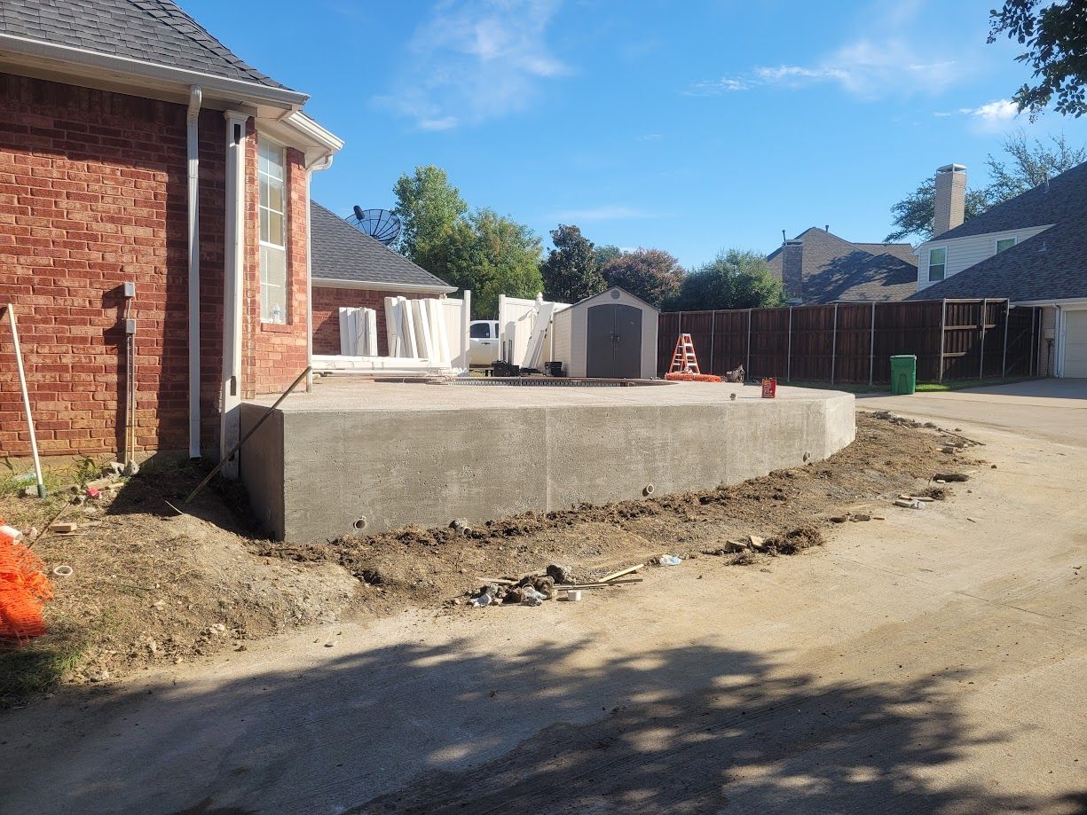 Brick house backyard with a large raised concrete slab and dirt driveway under construction