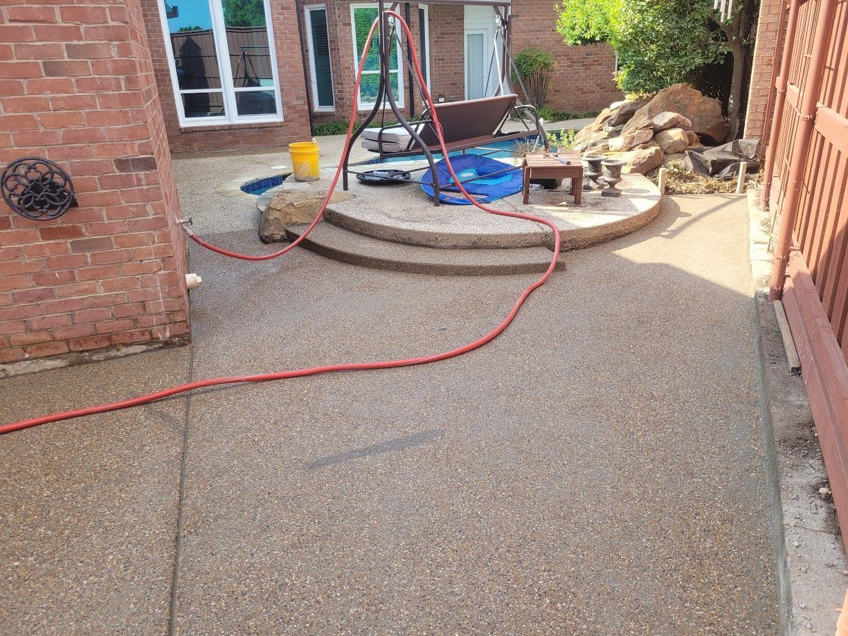 Backyard patio with wet concrete, red hose, and a wheelbarrow near brick walls
