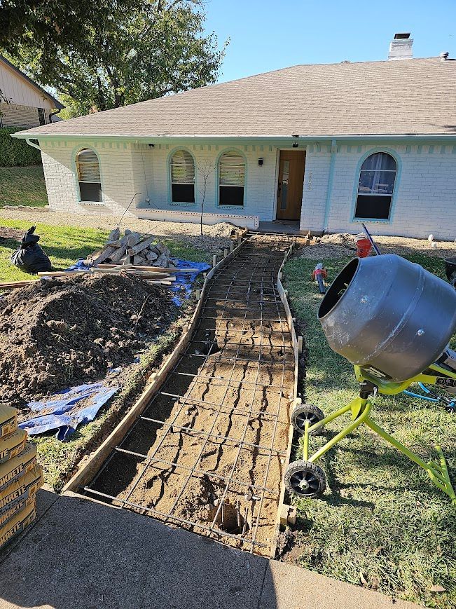 Backyard with concrete walkway forms and rebar, plus a cement mixer beside a house under construction