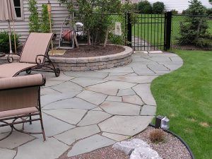 Backyard stone patio with curved walkway, fire pit, lounge chairs, and green lawn