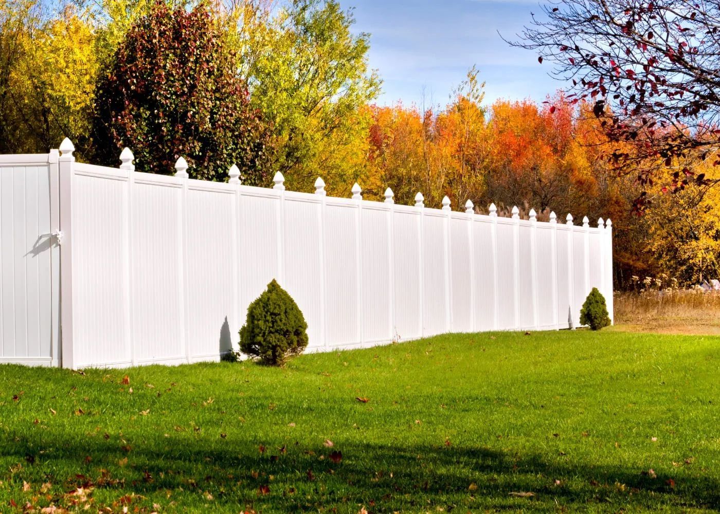 White vinyl fence along a green lawn with autumn trees in the background
