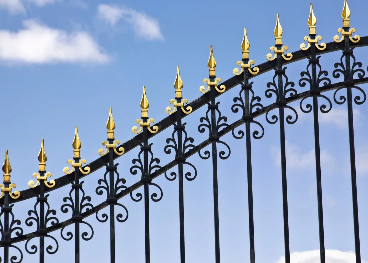 Black wrought-iron fence with gold finials against a blue sky