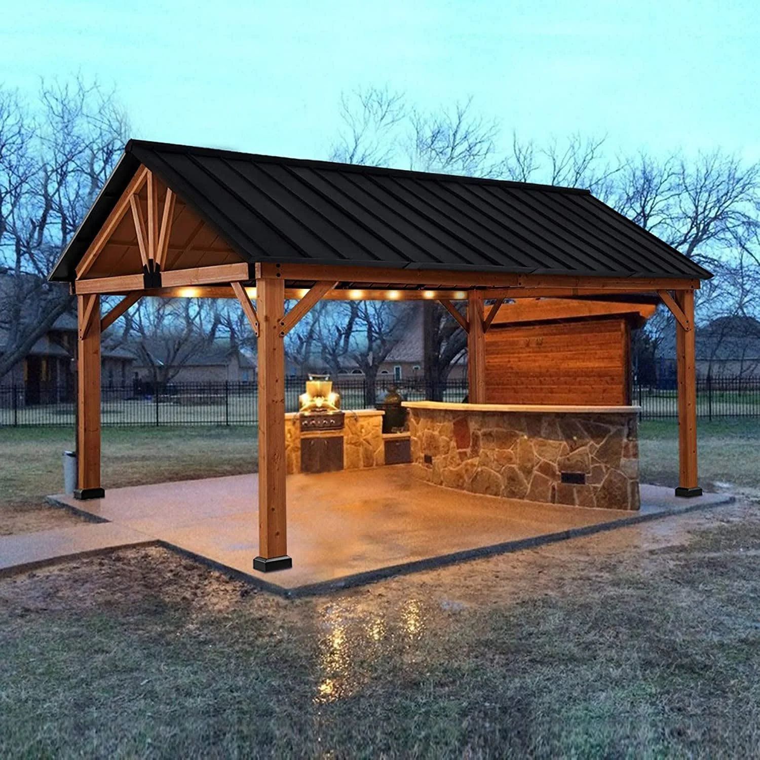 Wooden pavilion shelter with stone grill in a park at dusk, lit from within