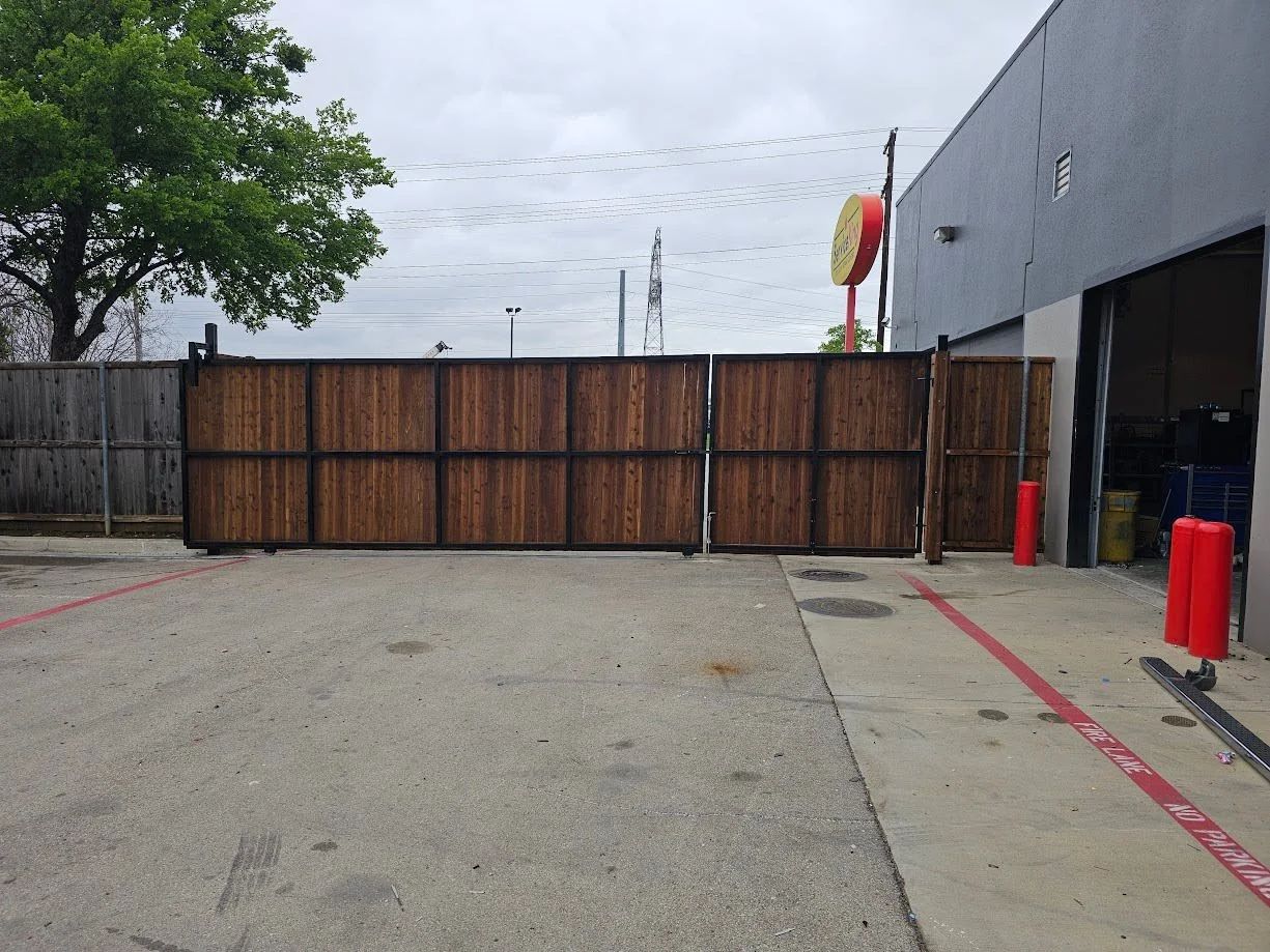 Closed wooden gate across an industrial driveway beside a gray building and red bollards