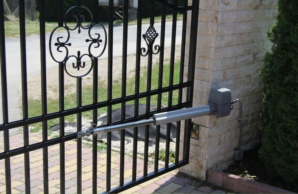 Motorized gate arm attached to a black metal driveway gate by a brick wall