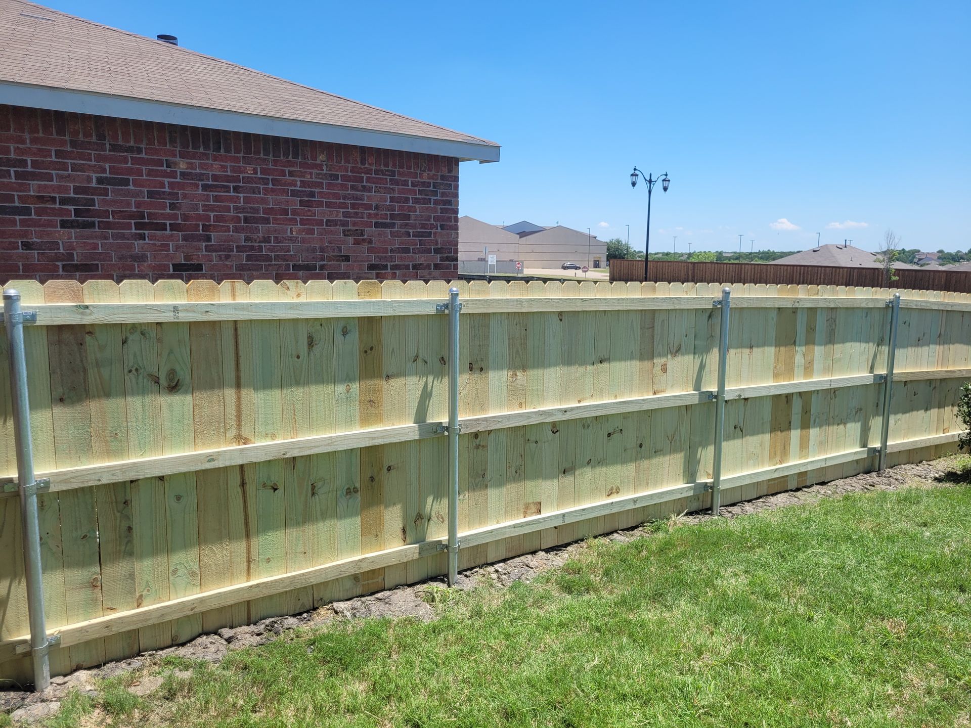 New wooden backyard fence beside a brick house under a clear blue sky.