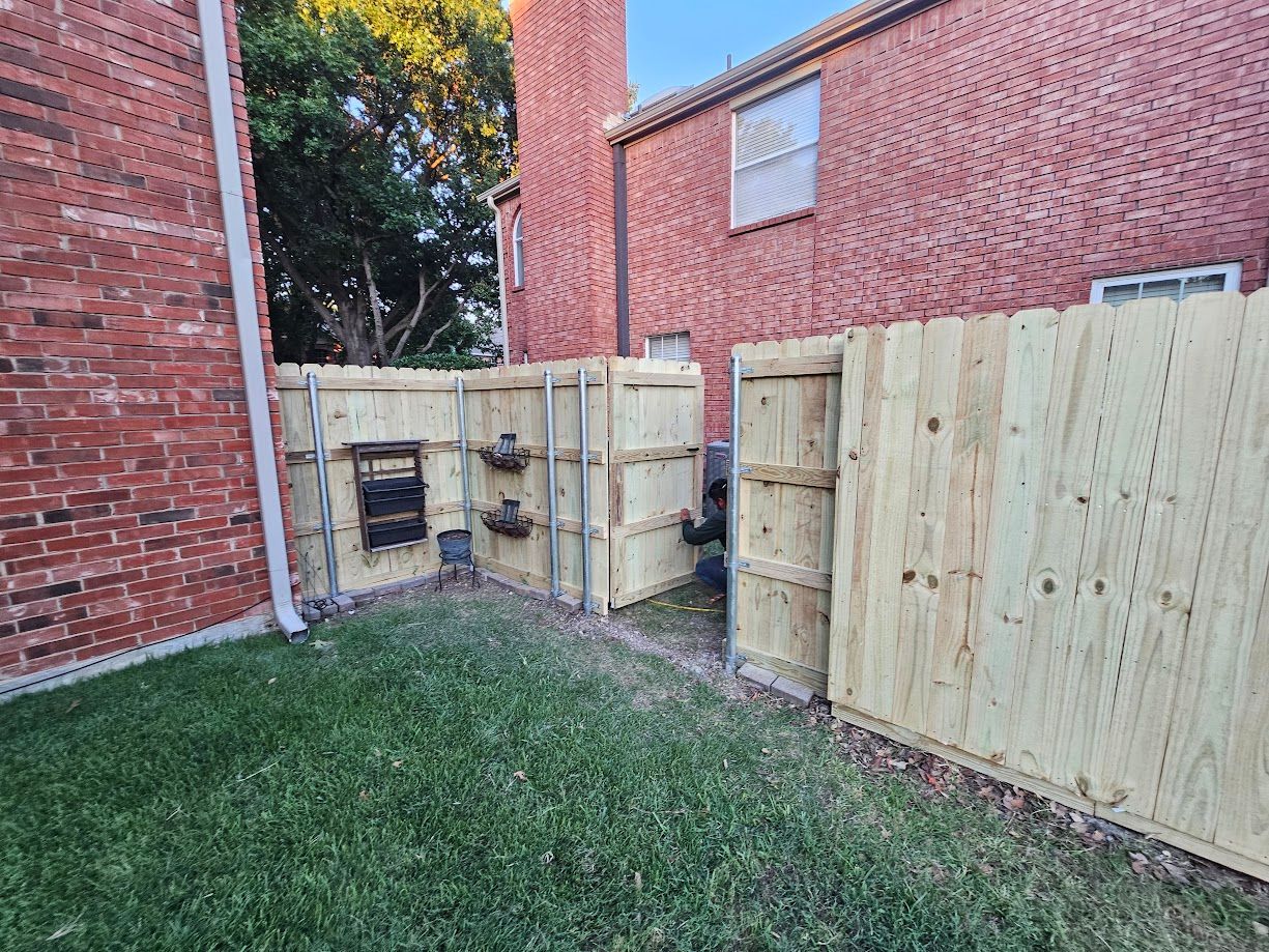 Backyard corner with brick walls, grass, and a new wooden fence and gate around utility equipment