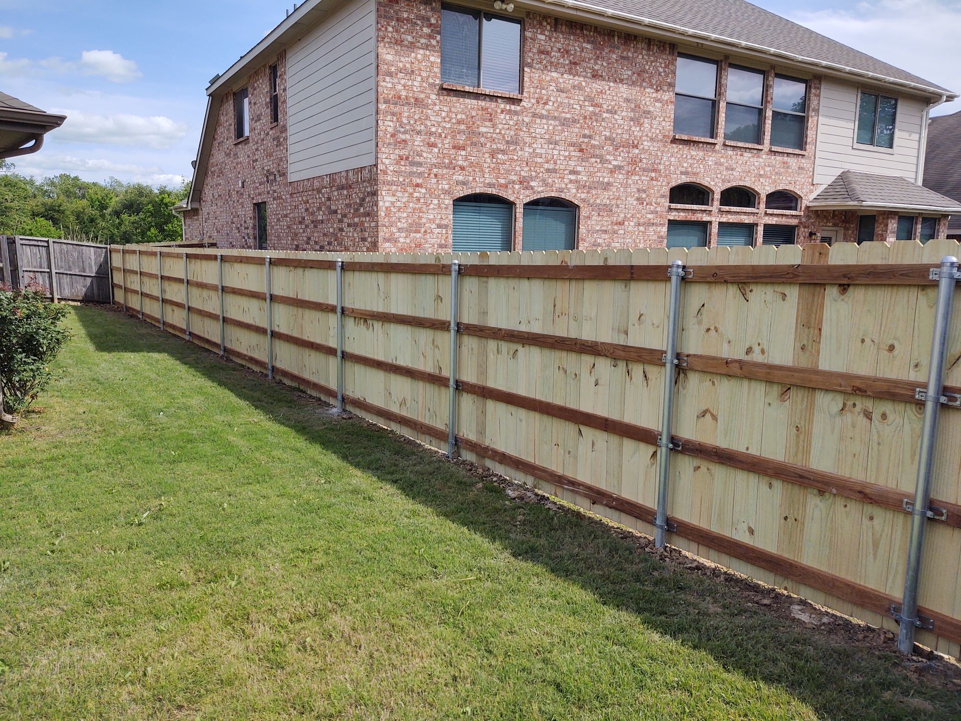 Backyard with a long wooden fence beside a brick house and grassy lawn