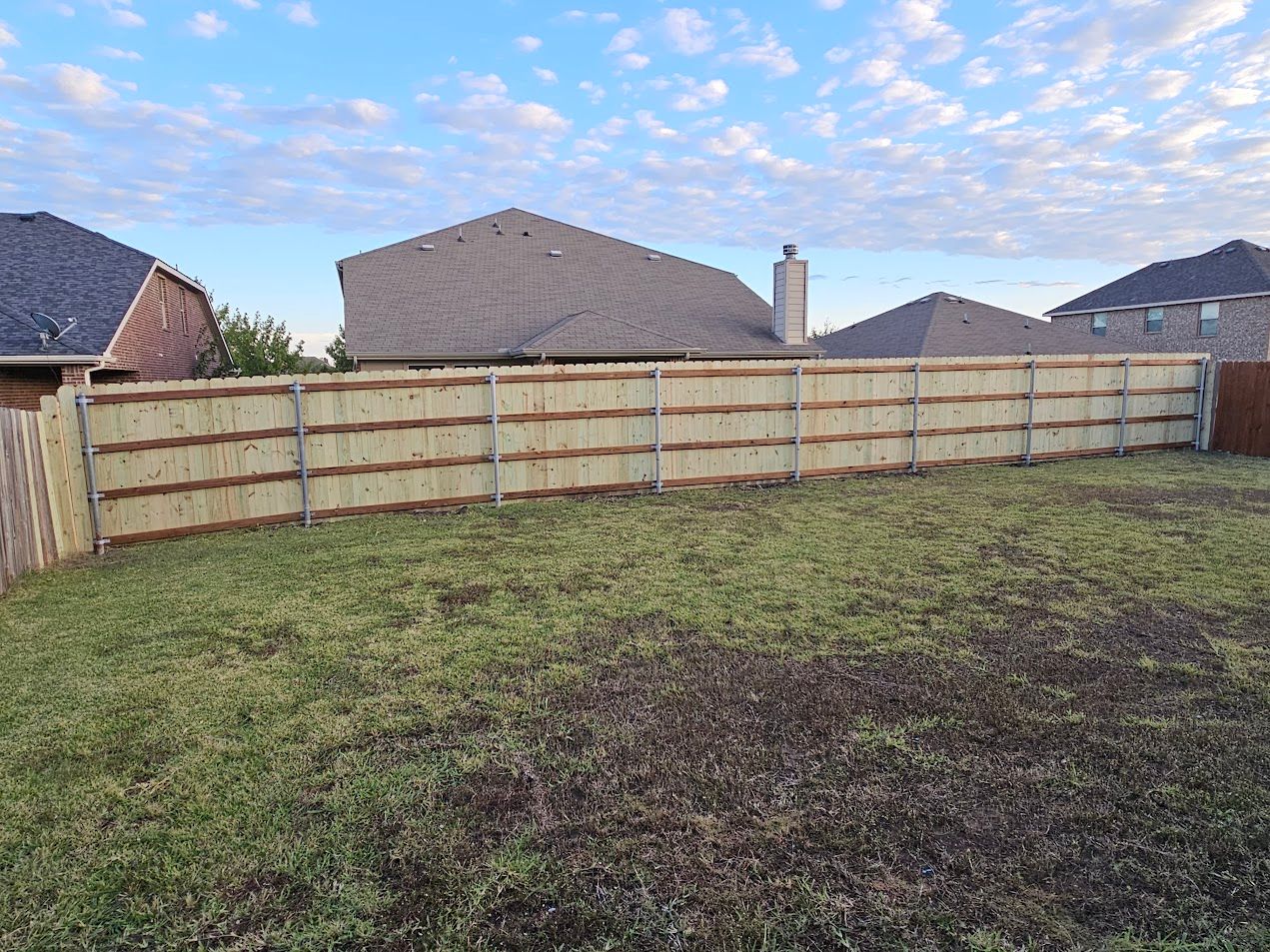 Backyard with a wooden privacy fence and grassy yard, with houses visible beyond the fence