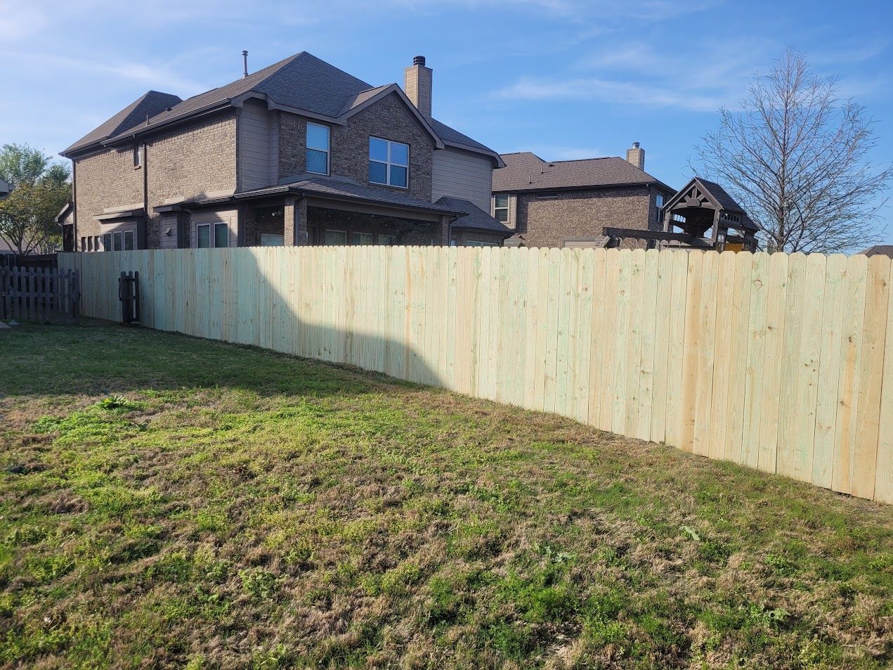 Backyard with fresh wooden fence in front of stone houses and a grassy lawn under a blue sky