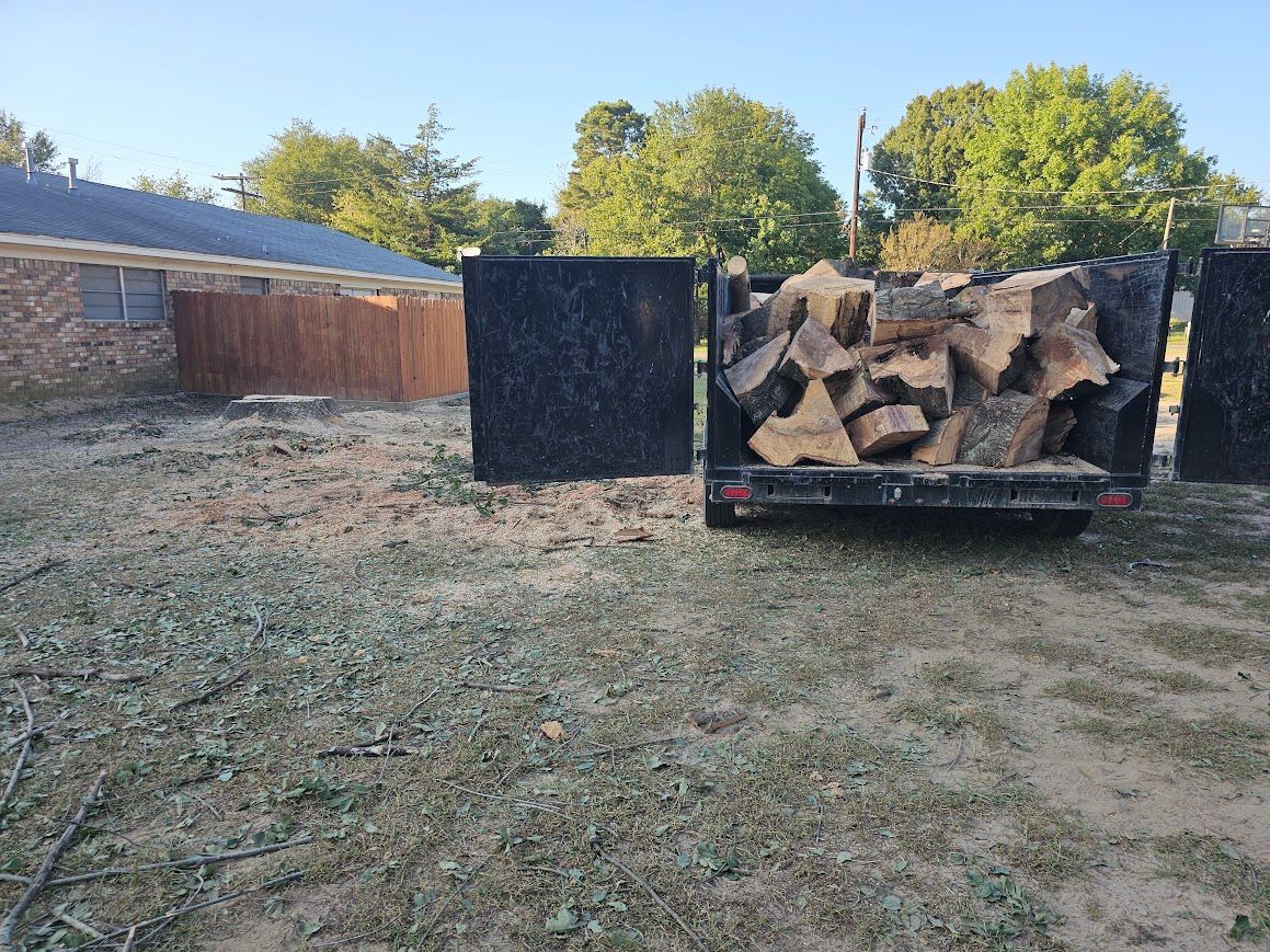 Trailer loaded with chopped wood in a frosty yard beside a brick house and wooden fence