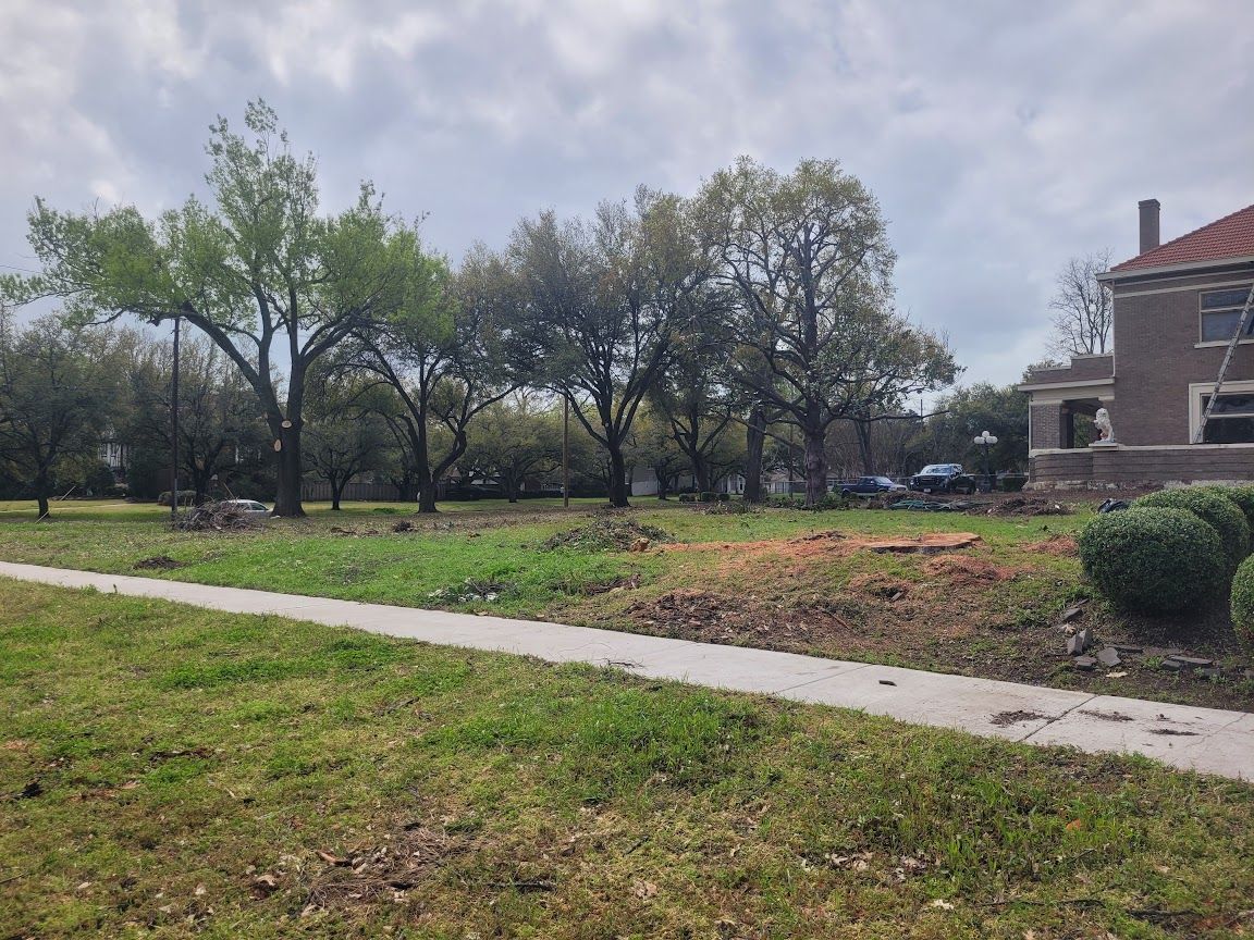 Park with sidewalk, grassy lawn, trees, and a brick house under cloudy skies