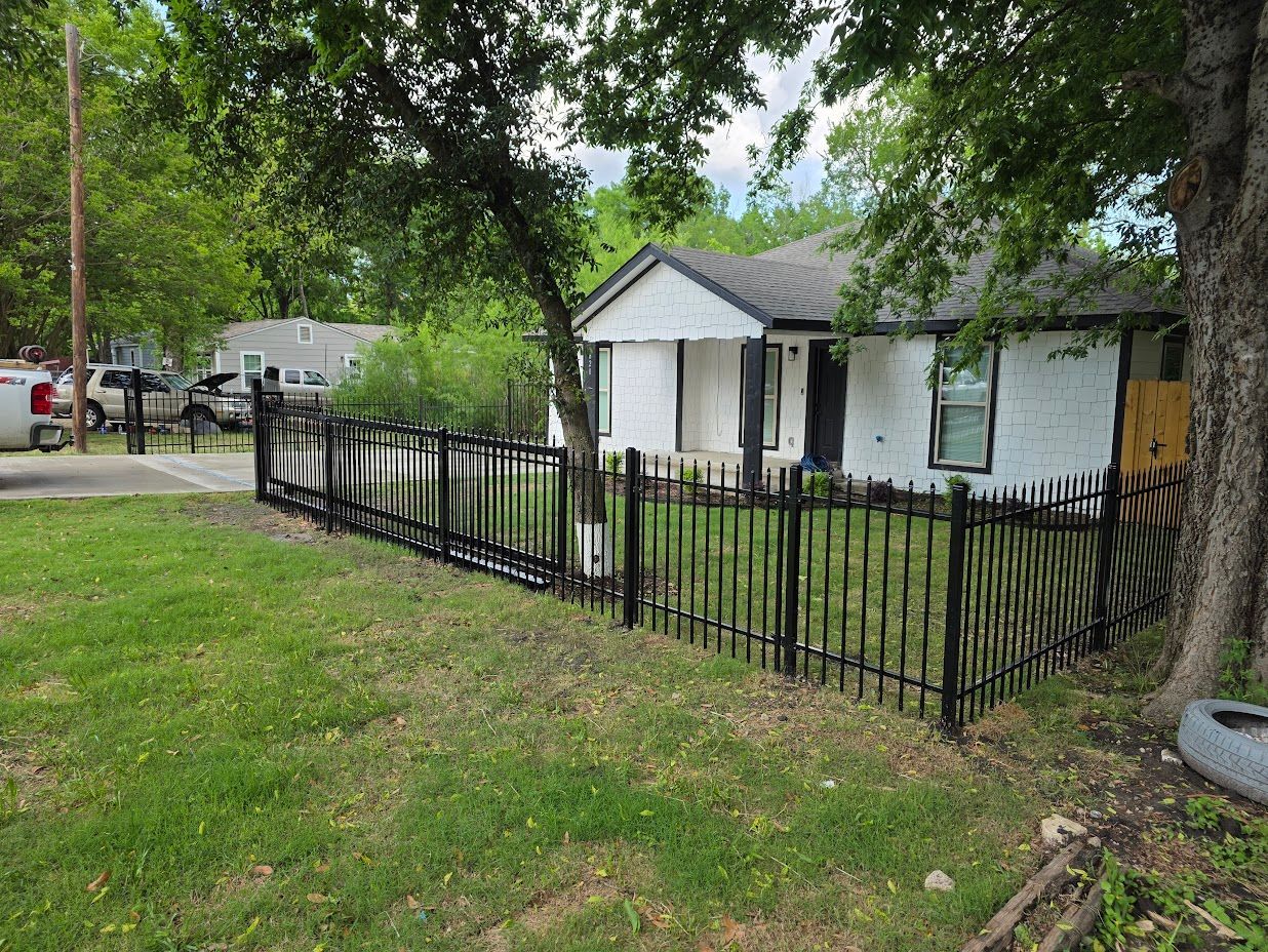 Small white house with a black fence and green yard under trees