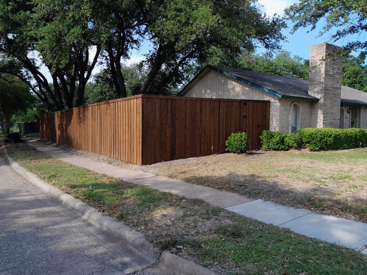 Wooden privacy fence beside a suburban house with a stone chimney and sidewalk along the street
