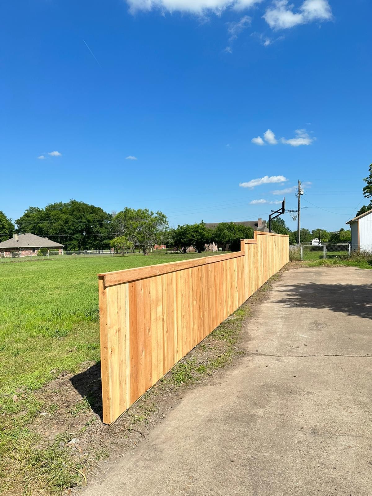 Wooden fence along a dirt path beside a grassy field under a blue sky
