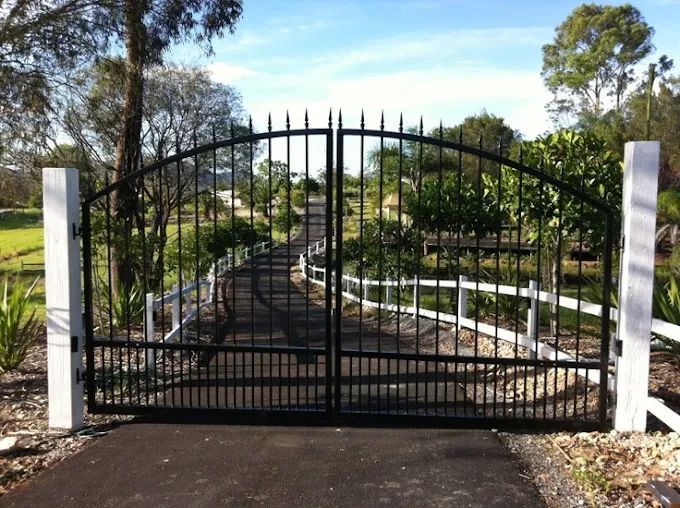 Black wrought-iron gate at the entrance to a tree-lined path in a park or garden.