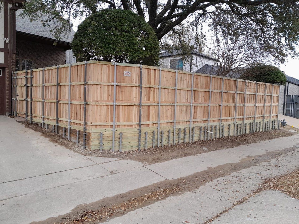 Large wooden construction fence enclosing a corner lot beside a street and sidewalk.