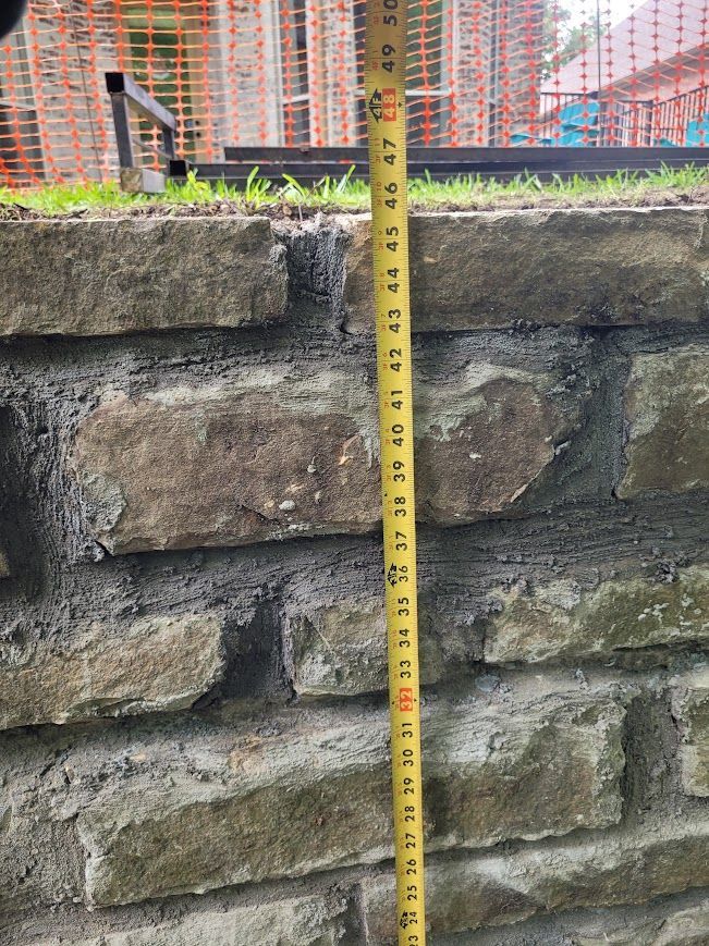 Yellow measuring tape against a weathered stone wall, with a construction site in the background