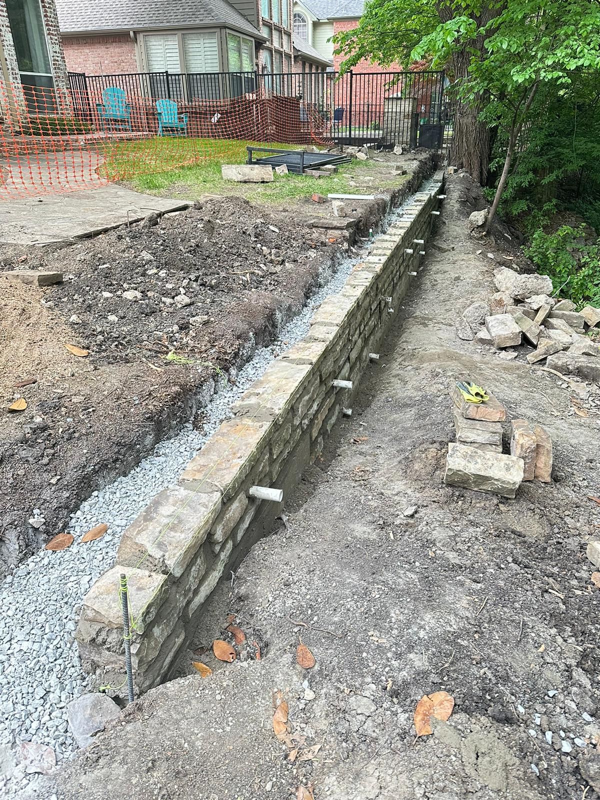 Construction site with a long concrete drainage trench beside gravel and a house