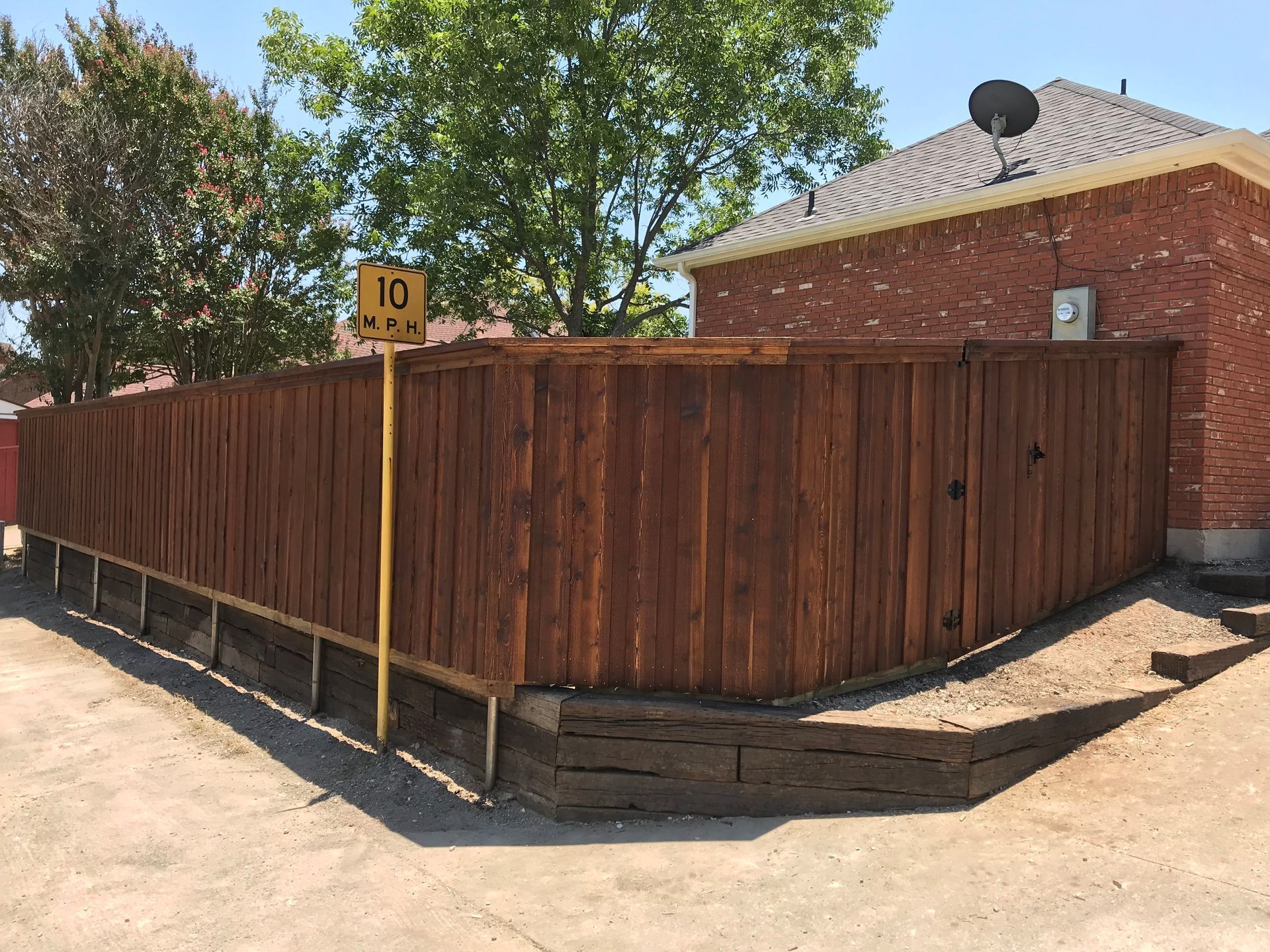 Wooden privacy fence around a brick house with a yellow post marker and trees in the yard