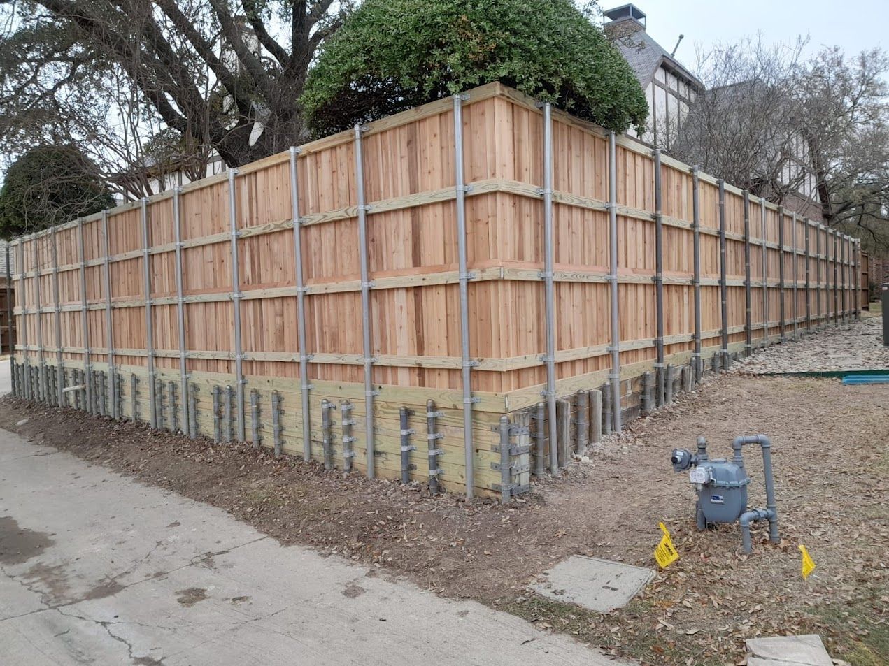 Long wooden privacy fence around a yard, with trees overhead and a sidewalk along the side
