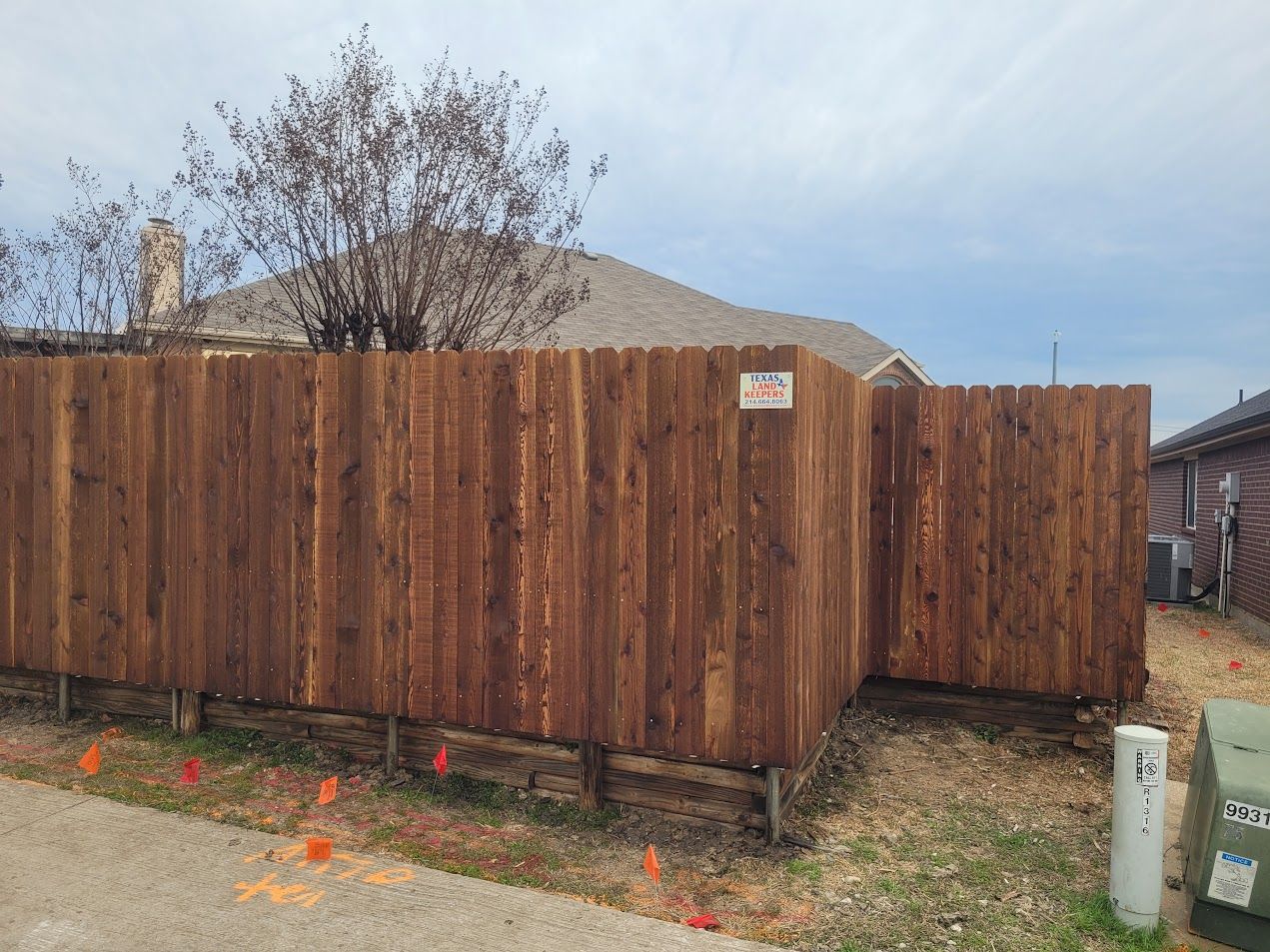 Wooden privacy fence around a yard, with dry grass and a cloudy sky.