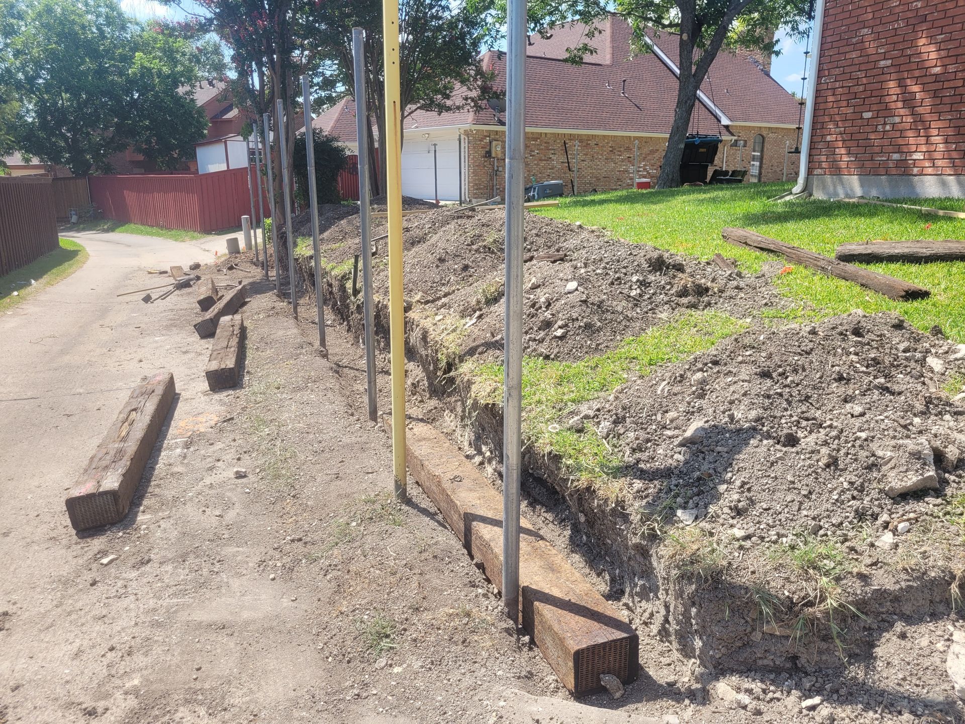 Backyard construction path with dirt piles, metal posts, and brick houses in the background