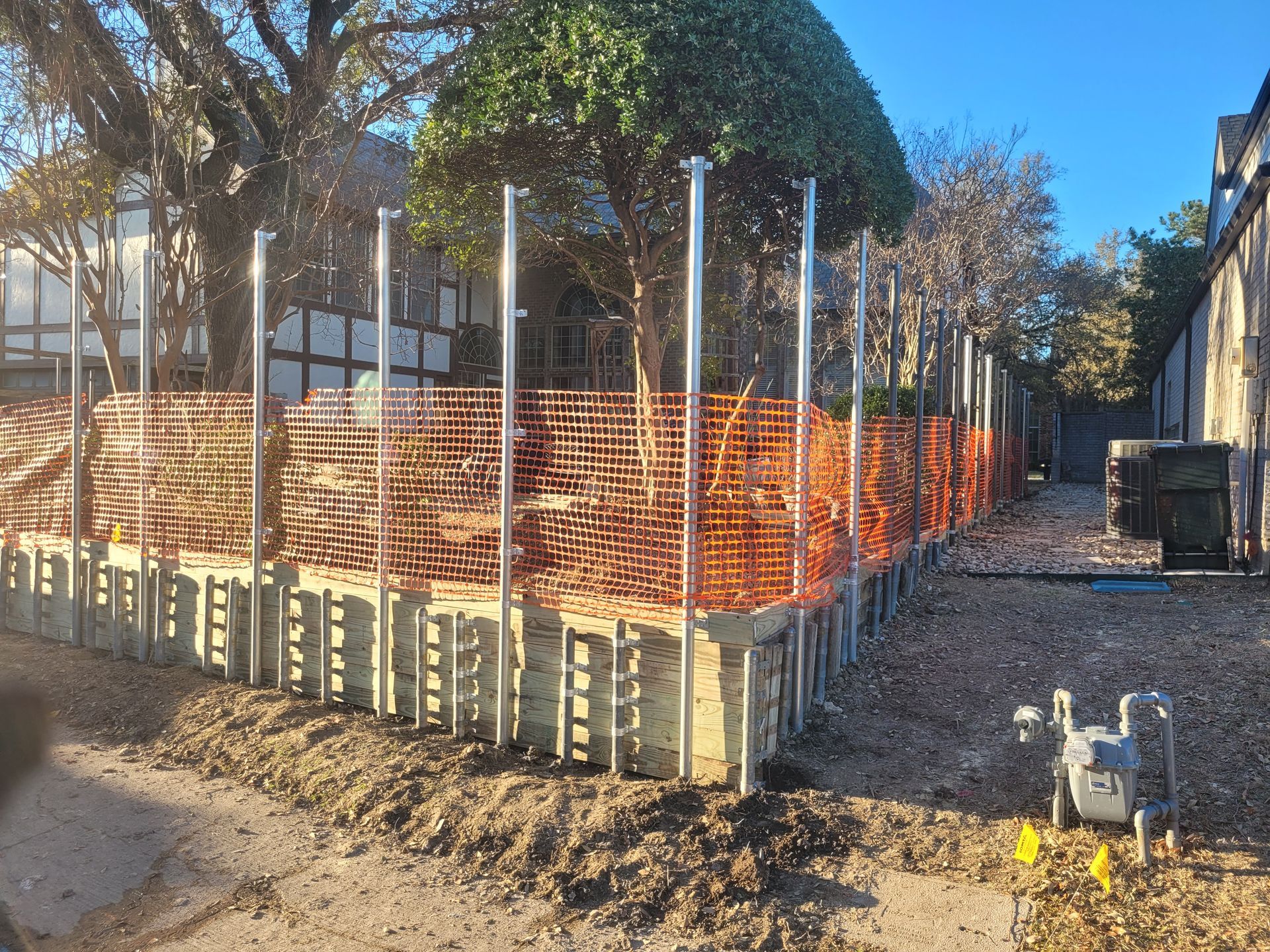 Construction site with a small concrete foundation, orange safety fencing, and metal posts under a sunny sky