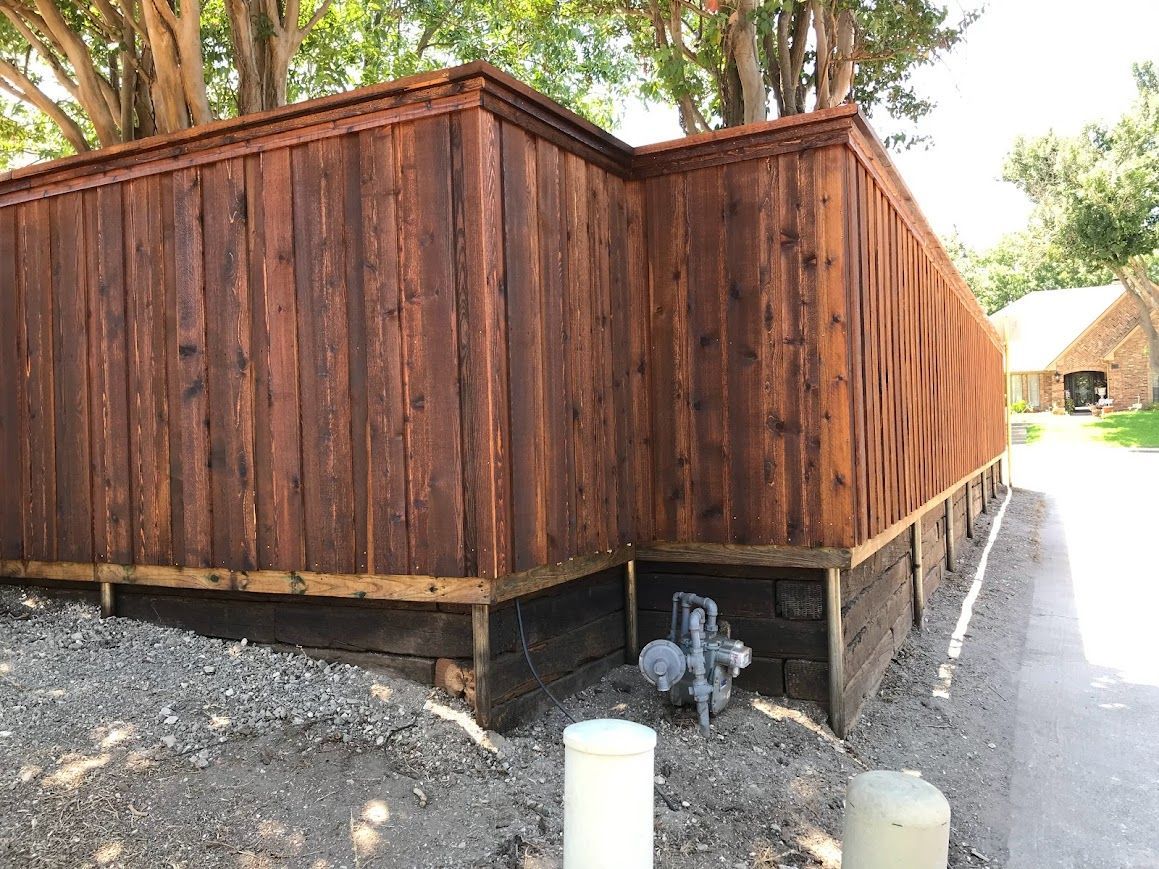 Wooden shed or small building with a dark foundation beside a gravel path and trees