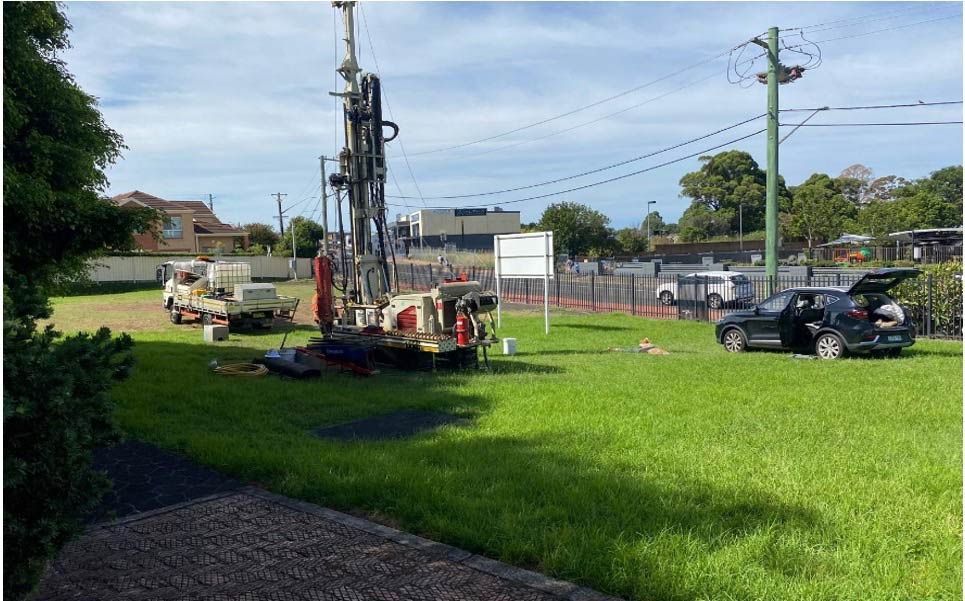 A car is parked in a grassy field with a drill in the background.