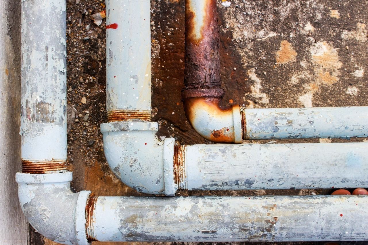 Rusty, light-blue painted pipes and connectors on a weathered concrete wall.