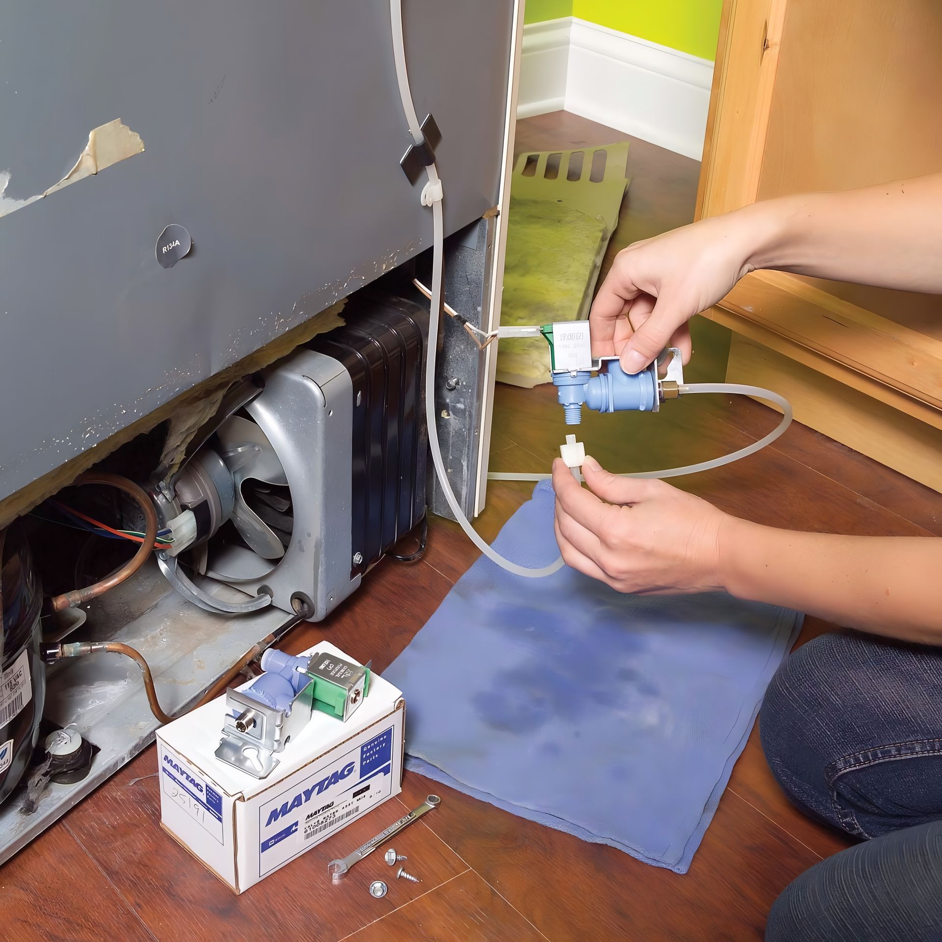 Person repairing a refrigerator water valve, with replacement parts on the floor. They are connecting a tube to the valve.