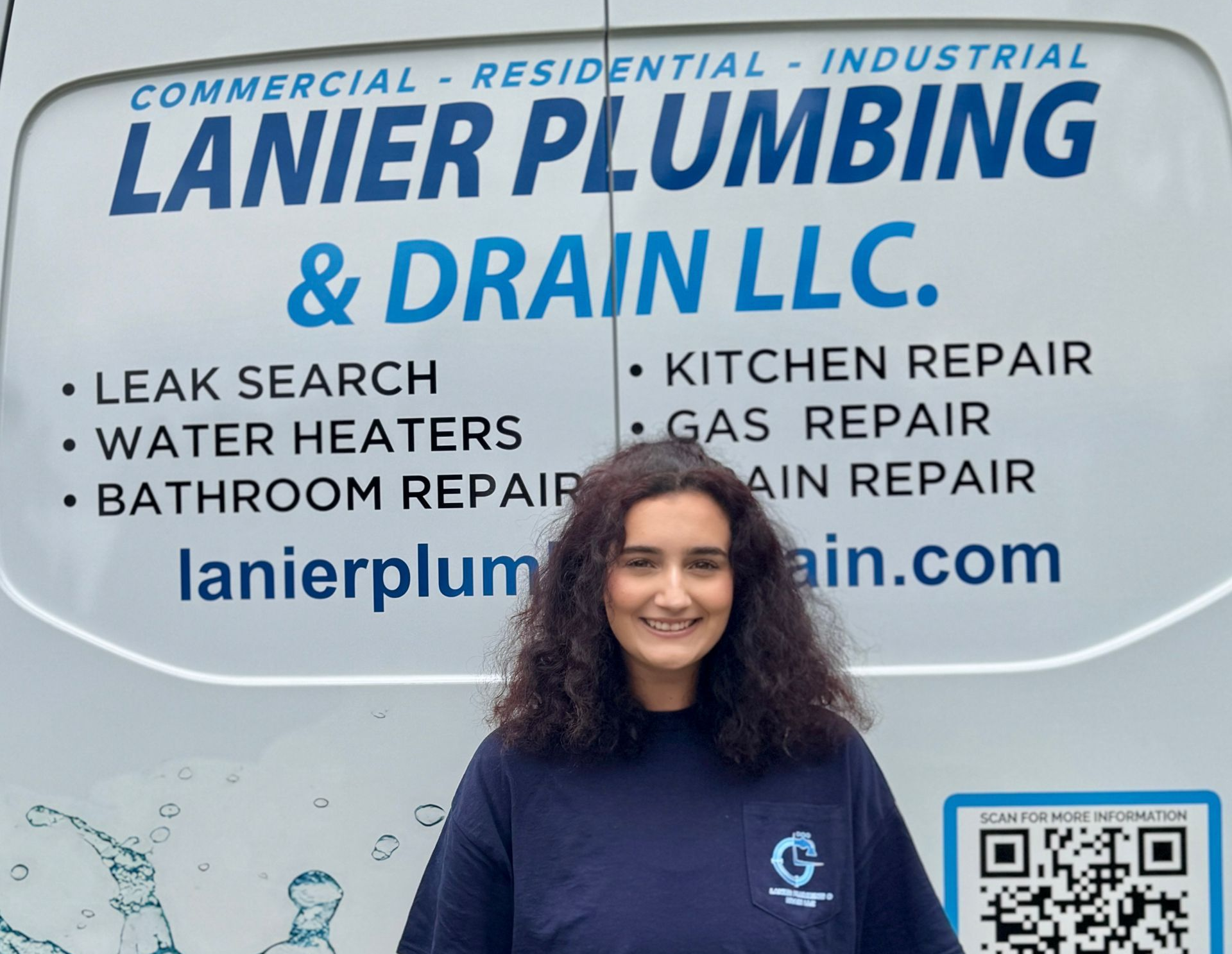 Woman standing in front of Lanier Plumbing & Drain LLC truck sign with service list and QR code