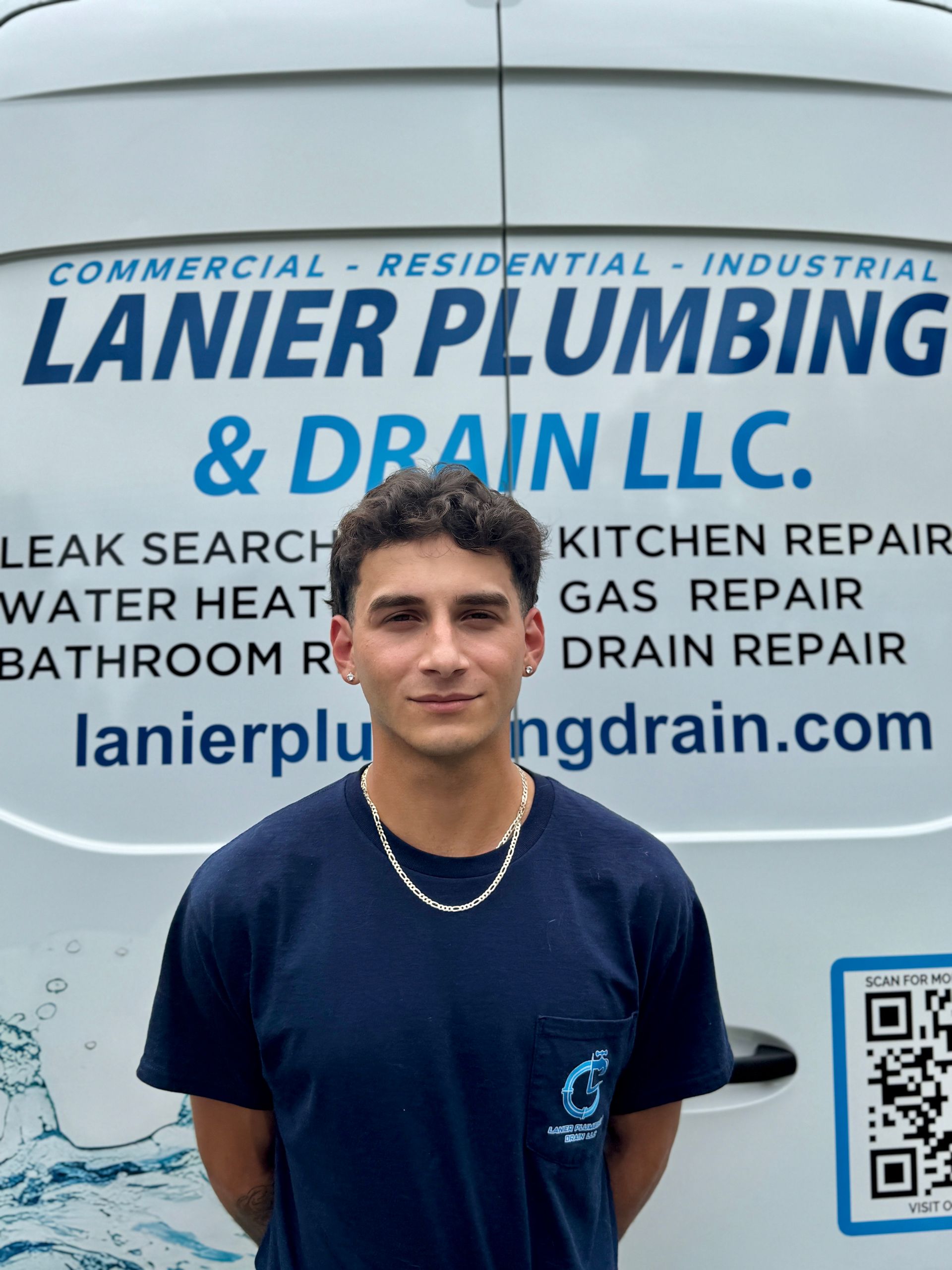 Young man in a navy shirt standing before a Lanier Plumbing & Drain LLC service van
