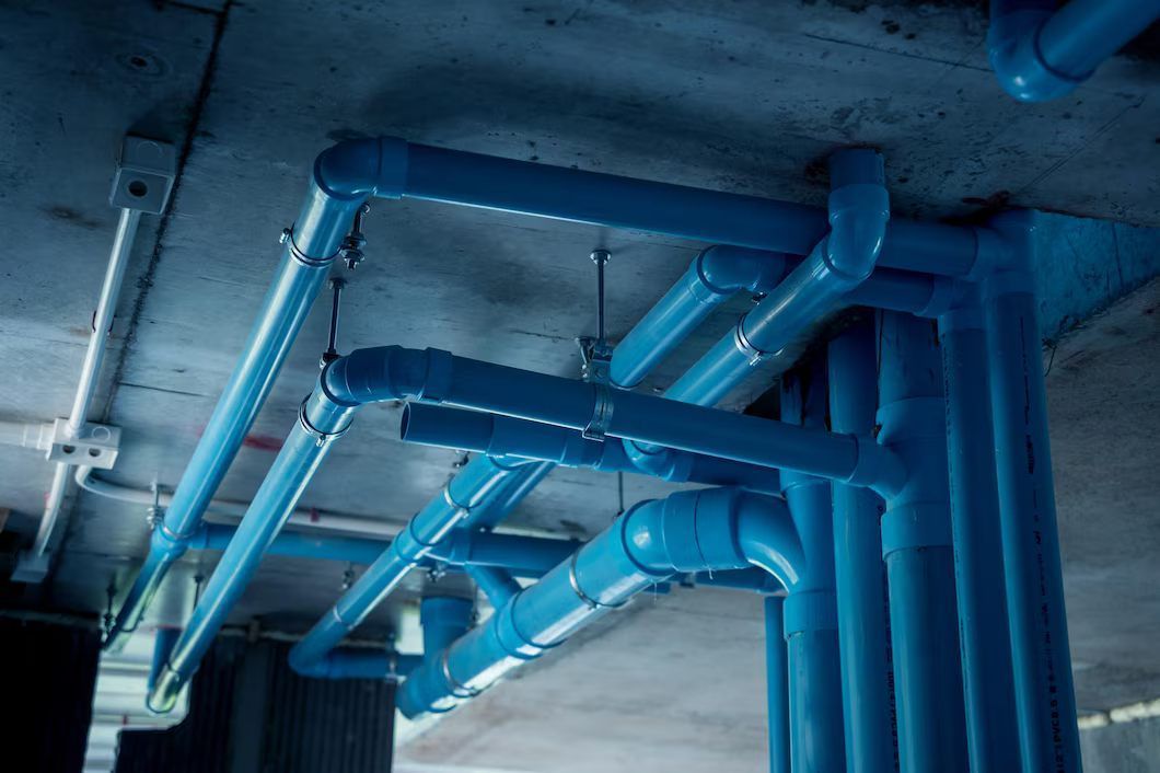 Blue pipes run along a concrete ceiling and down a support column. The pipes are connected with elbows and brackets.