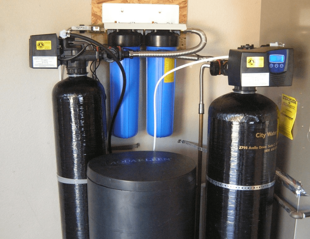 Water filtration system with black tanks, blue filter housings, and control boxes, mounted on a wall.