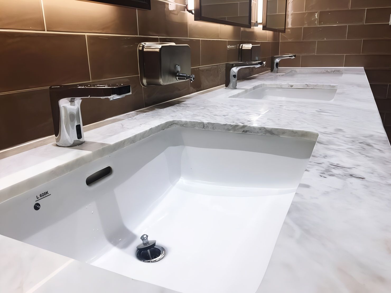 Accessible restroom sink with white marble countertop and stainless steel fixtures in a tiled wall setting